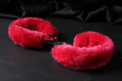 Photo of Red fluffy handcuffs and fabric on black surface, closeup