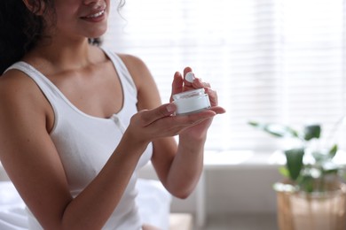 Woman with jar of cream at home, closeup. Space for text