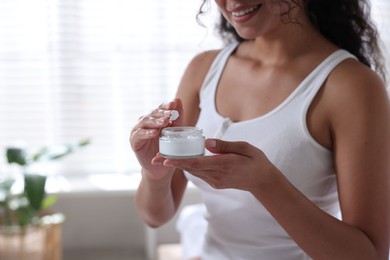 Woman with jar of cream at home, closeup. Space for text