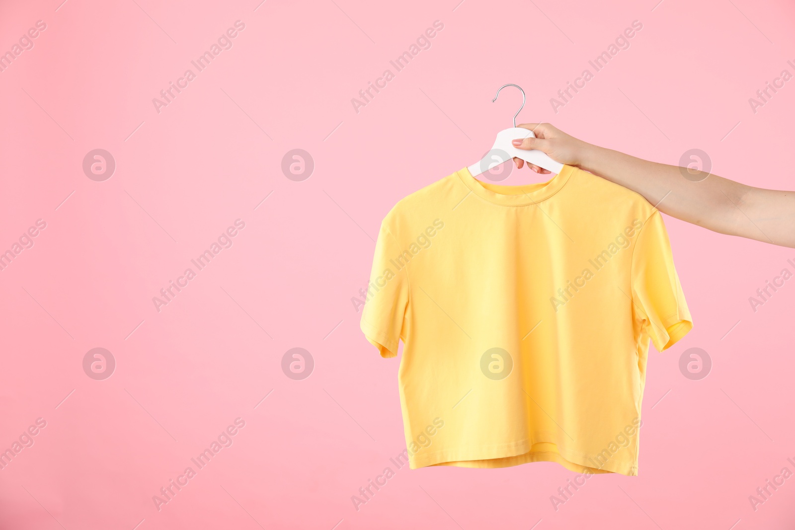 Photo of Woman holding hanger with yellow t-shirt on pink background, closeup. Space for text