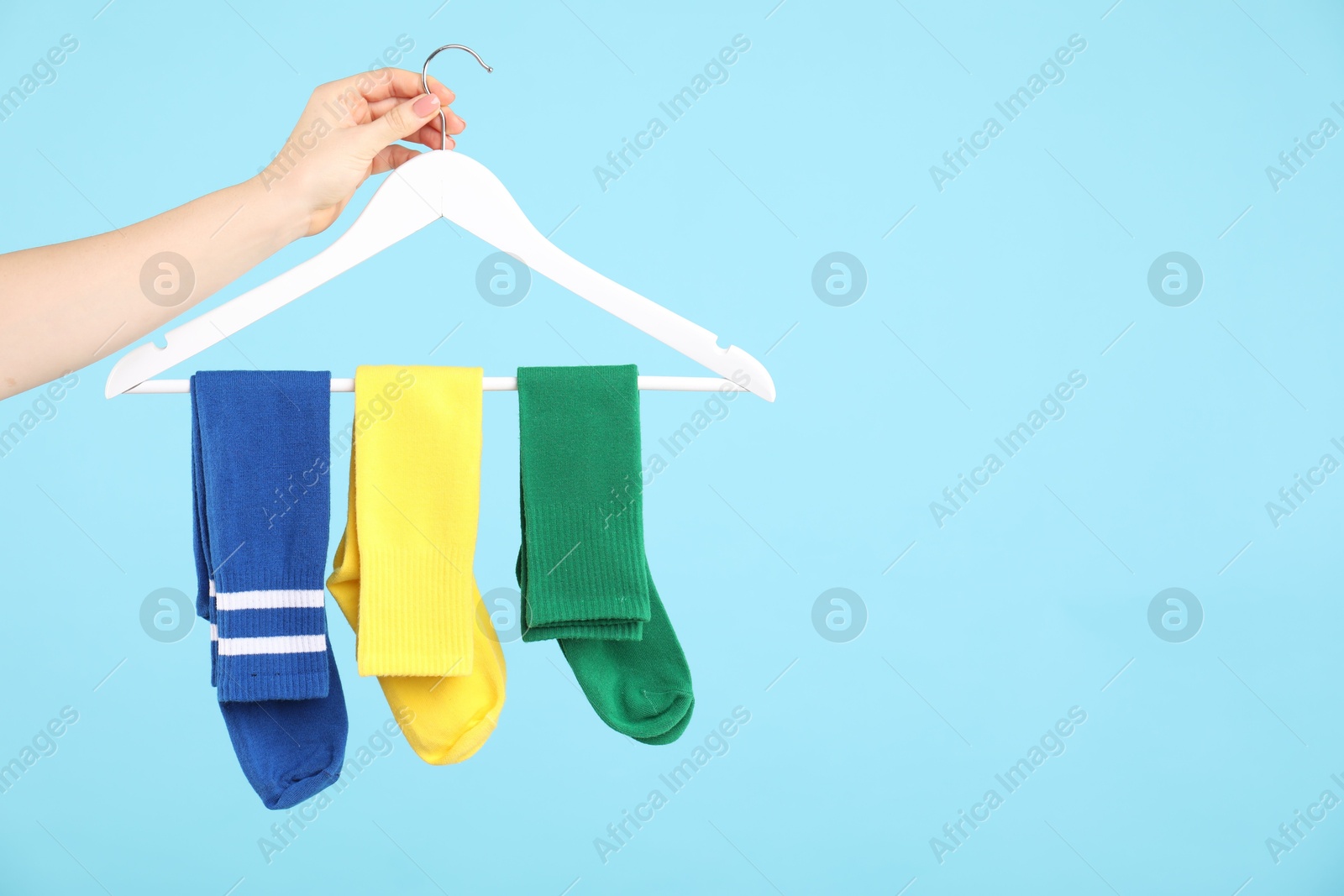 Photo of Woman holding hanger with bright socks on light blue background, closeup. Space for text