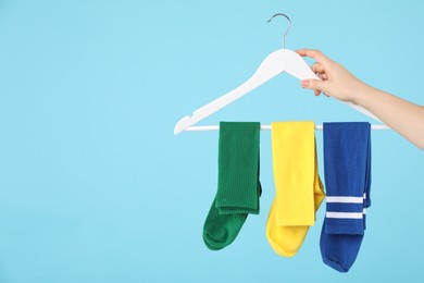 Photo of Woman holding hanger with bright socks on light blue background, closeup. Space for text