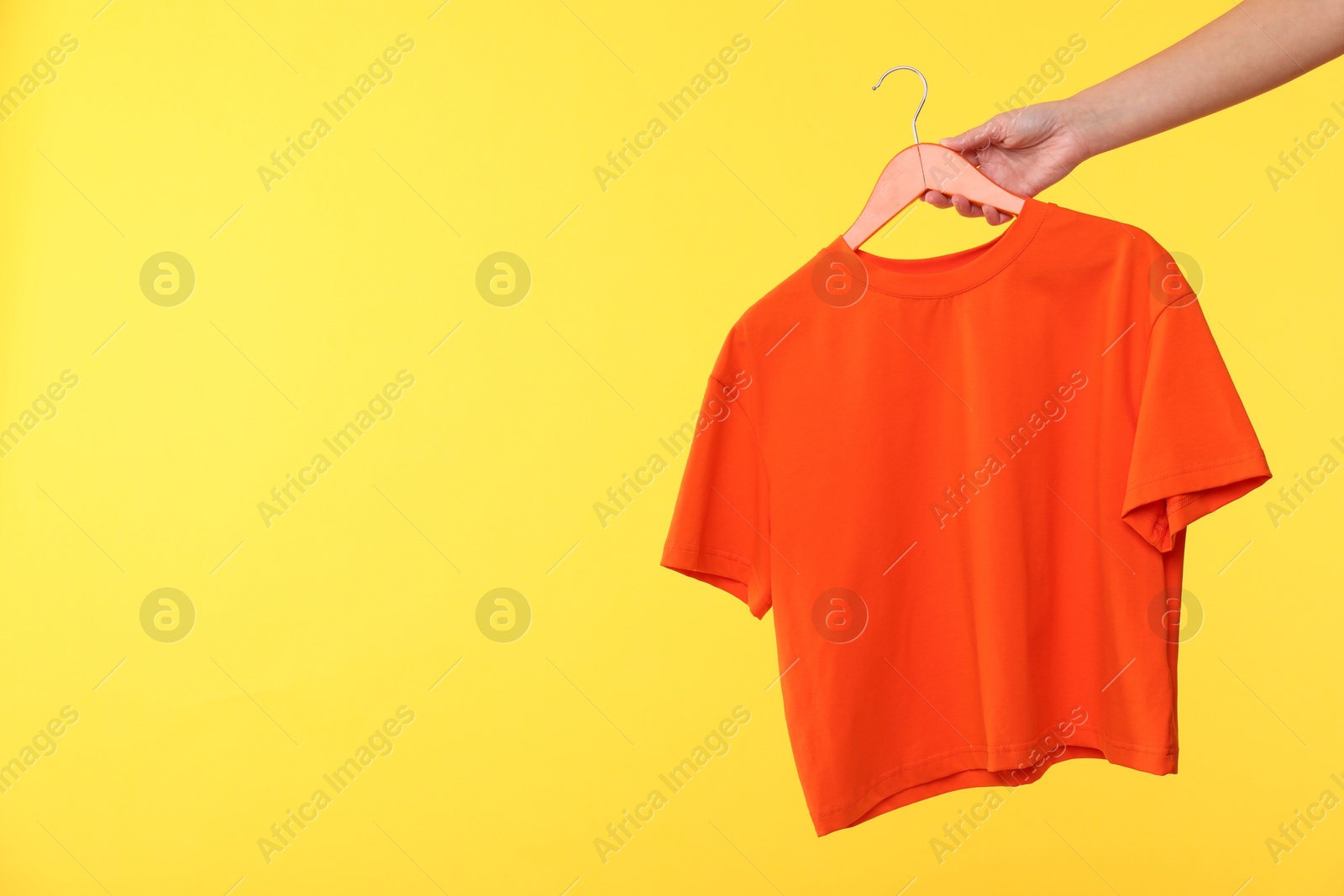 Photo of Woman holding hanger with t-shirt on yellow background, closeup. Space for text