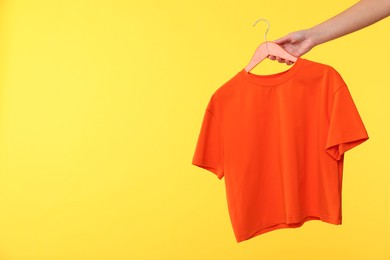 Photo of Woman holding hanger with t-shirt on yellow background, closeup. Space for text