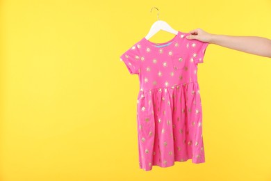 Photo of Woman holding hanger with pink baby dress on yellow background, closeup. Space for text