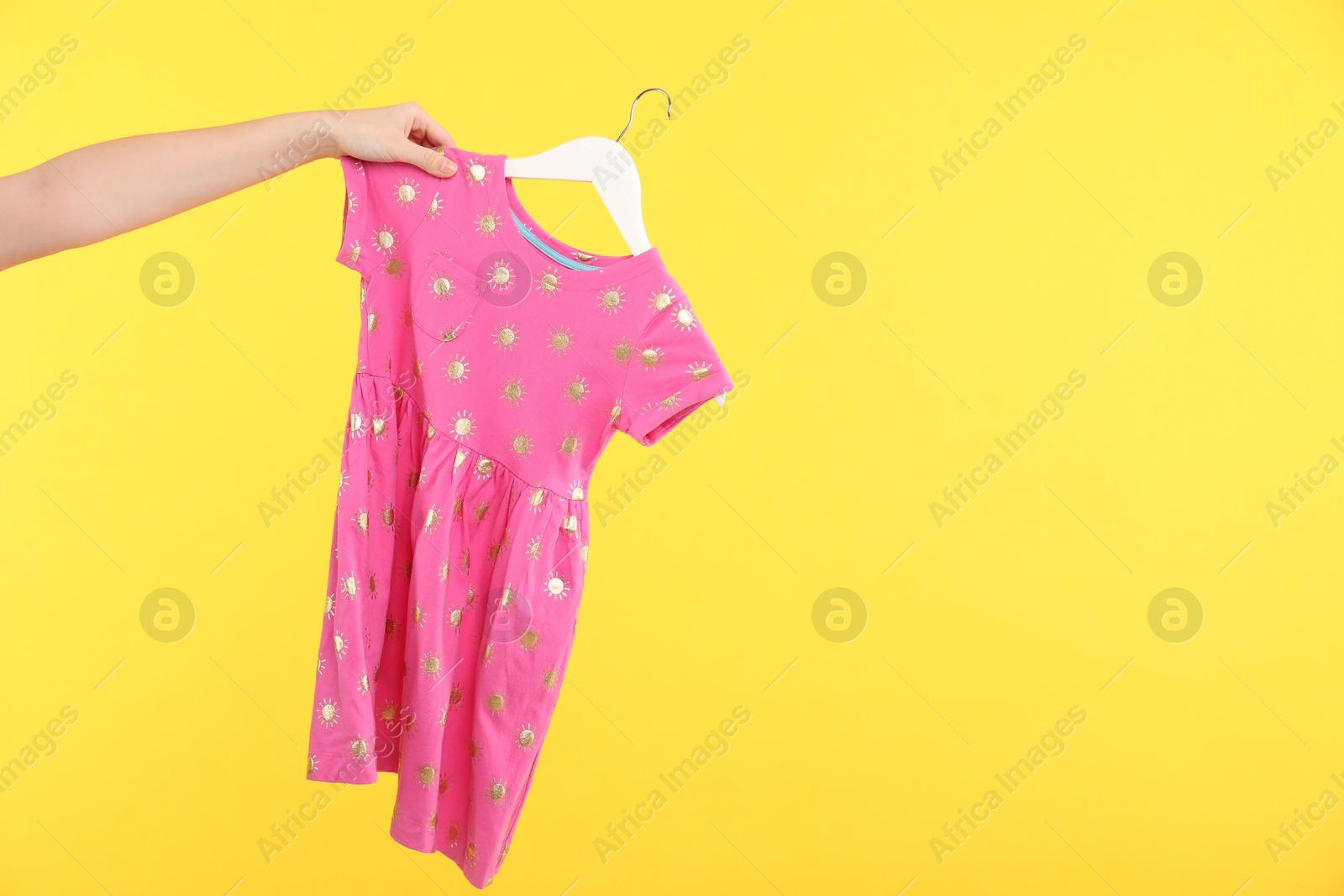 Photo of Woman holding hanger with pink baby dress on yellow background, closeup. Space for text