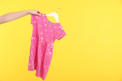 Photo of Woman holding hanger with pink baby dress on yellow background, closeup. Space for text