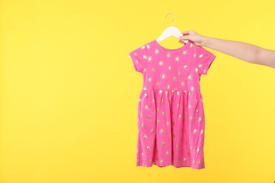 Photo of Woman holding hanger with pink baby dress on yellow background, closeup. Space for text