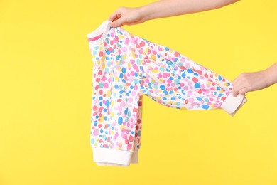 Photo of Woman holding beautiful baby sweater on yellow background, closeup