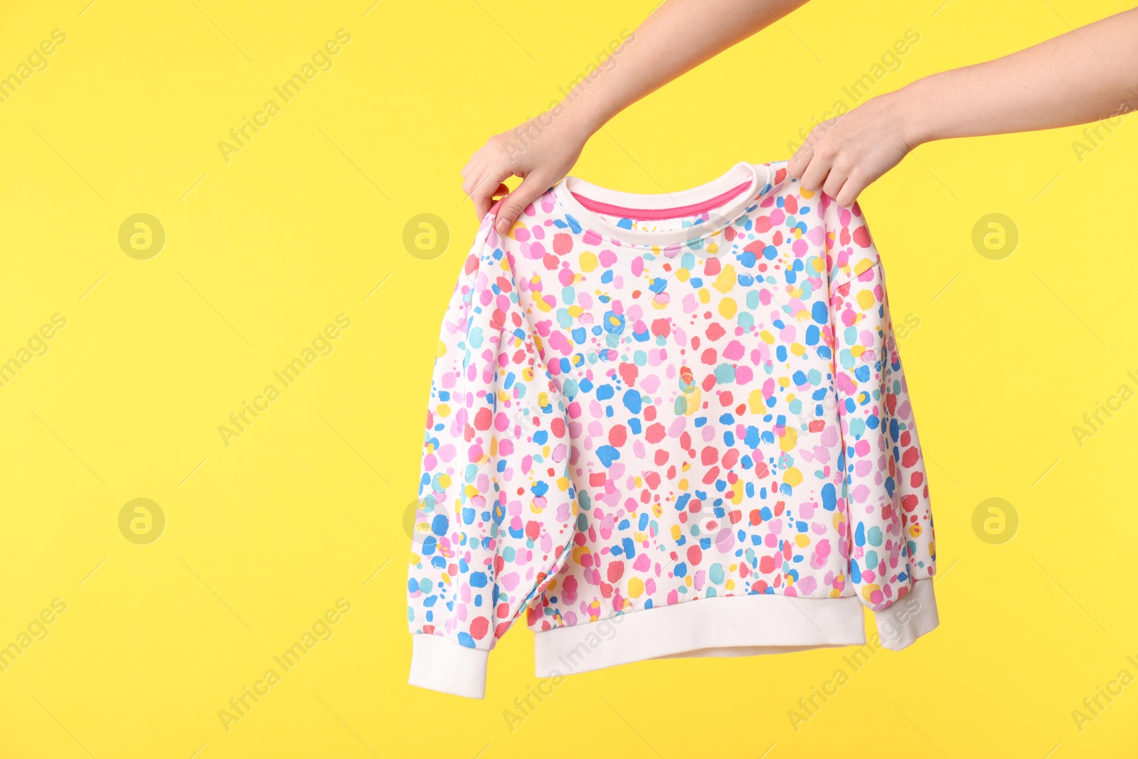 Photo of Woman holding beautiful baby sweater on yellow background, closeup. Space for text