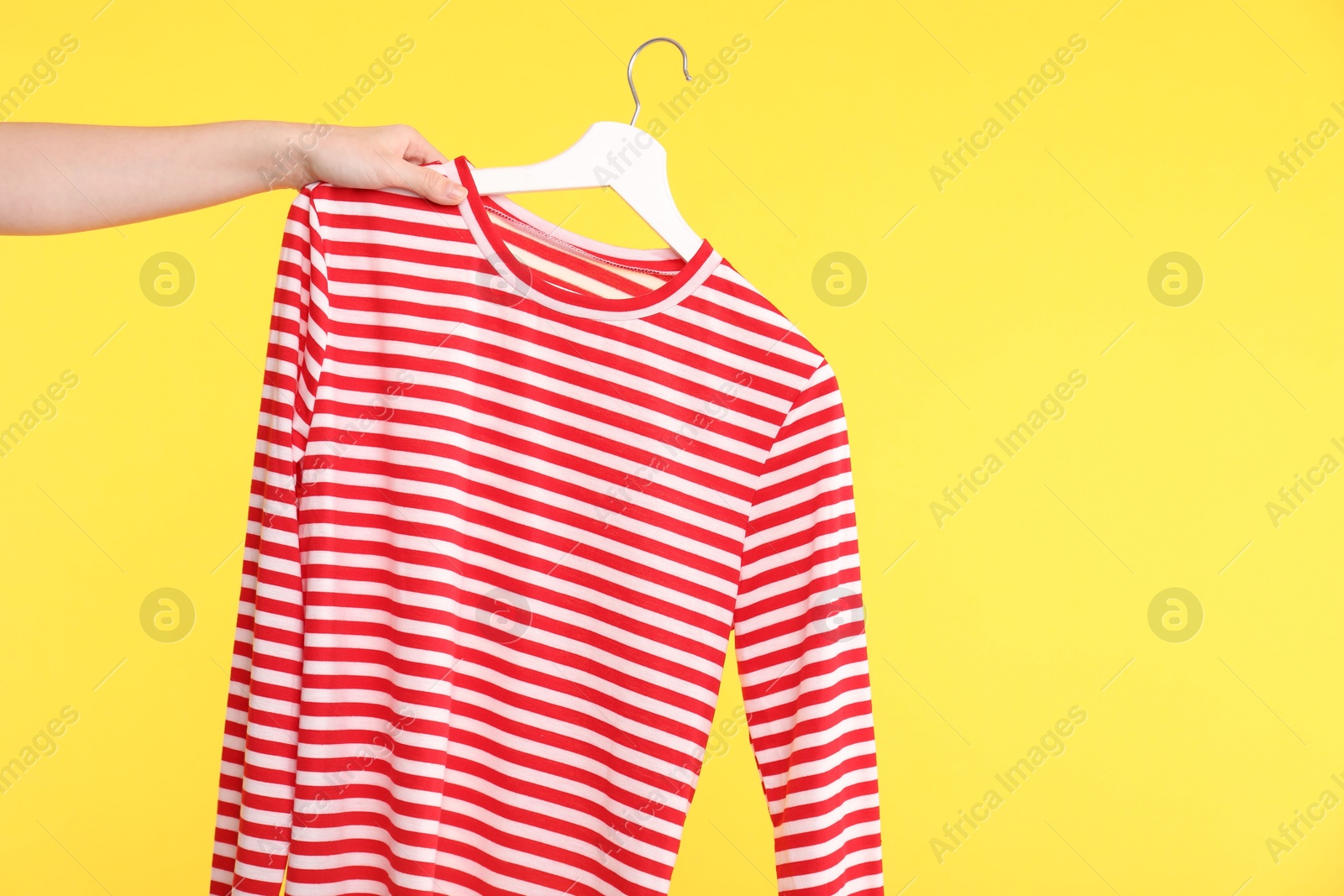 Photo of Woman holding striped long sleeve on yellow background, closeup. Space for text