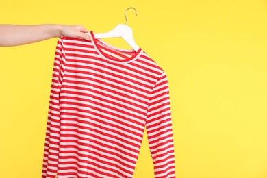 Photo of Woman holding striped long sleeve on yellow background, closeup. Space for text