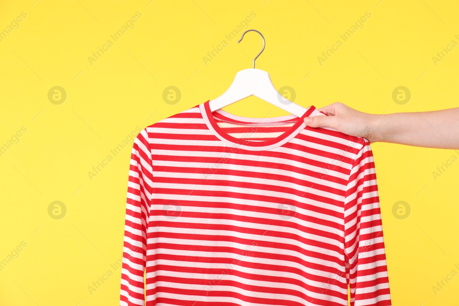 Photo of Woman holding hanger with striped long sleeve on yellow background, closeup