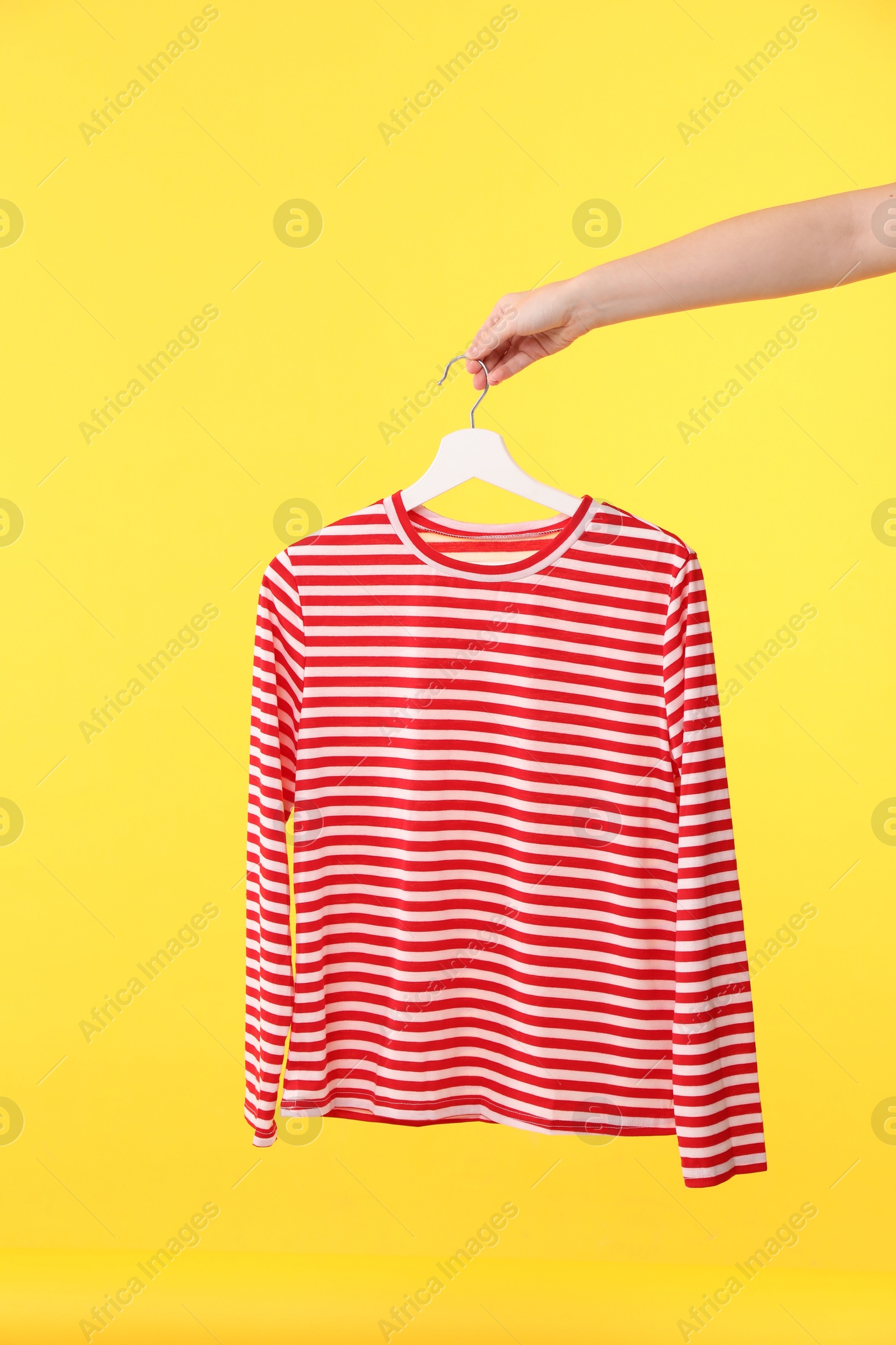 Photo of Woman holding hanger with striped long sleeve on yellow background, closeup