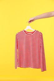 Photo of Woman holding hanger with striped long sleeve on yellow background, closeup