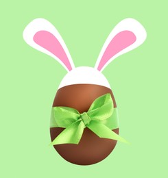 Illustration of Happy Easter. Chocolate egg with bunny ears and bow on light green background