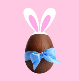 Illustration of Happy Easter. Chocolate egg with bunny ears and light blue bow on pink background