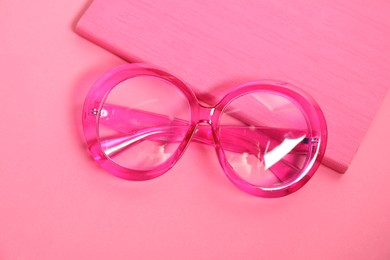 Stylish bright glasses and notebook on pink background, top view