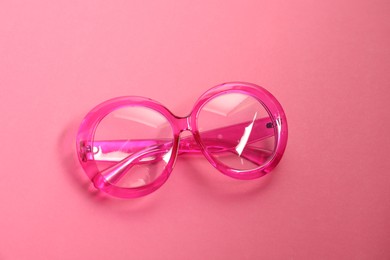 Stylish bright glasses on pink background, top view