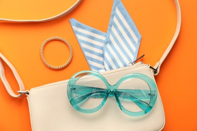 Photo of Stylish light blue glasses and other accessories on orange background, flat lay