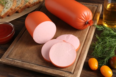 Photo of Tasty boiled sausages, ketchup, tomatoes, dill and bread on wooden table, closeup