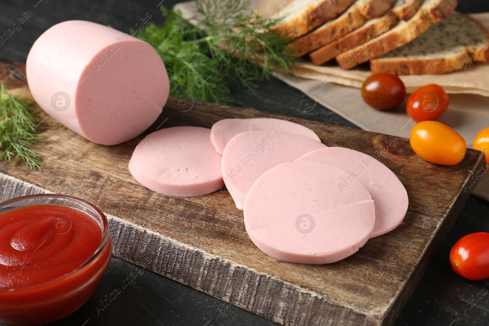 Photo of Tasty boiled sausage, tomatoes, dill, bread and ketchup on black table, closeup