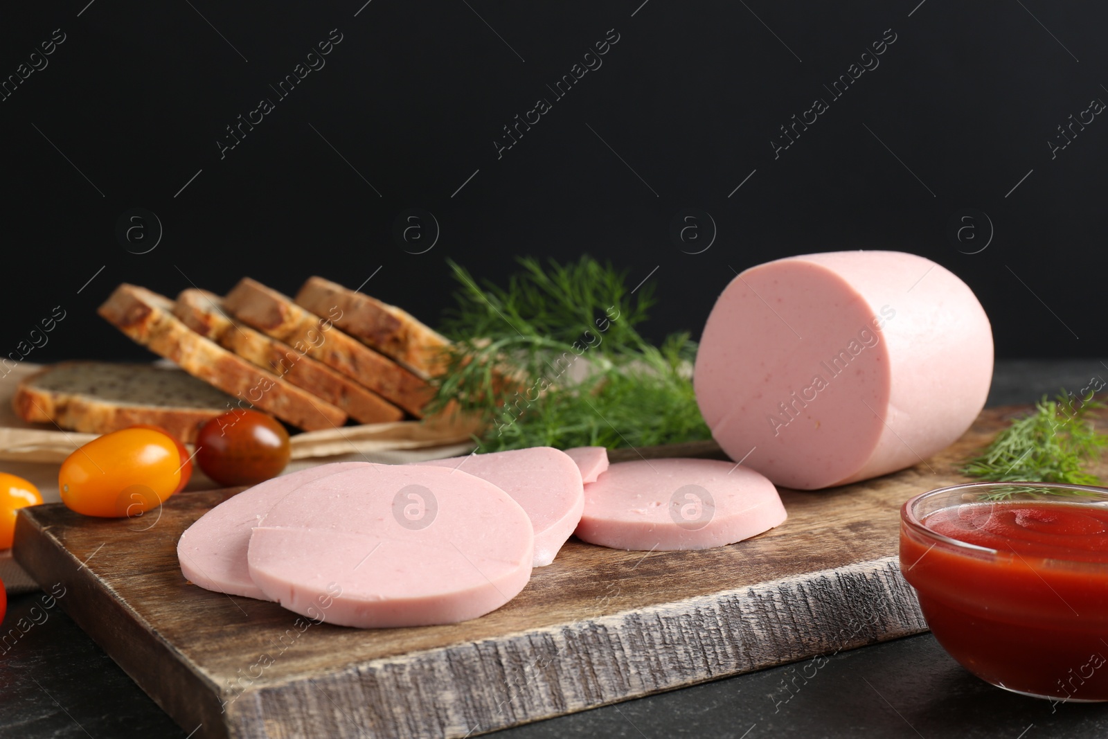 Photo of Tasty boiled sausage, tomatoes, dill, bread and ketchup on black table, closeup