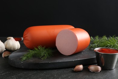 Photo of Tasty boiled sausages, ketchup, dill and garlic on black table