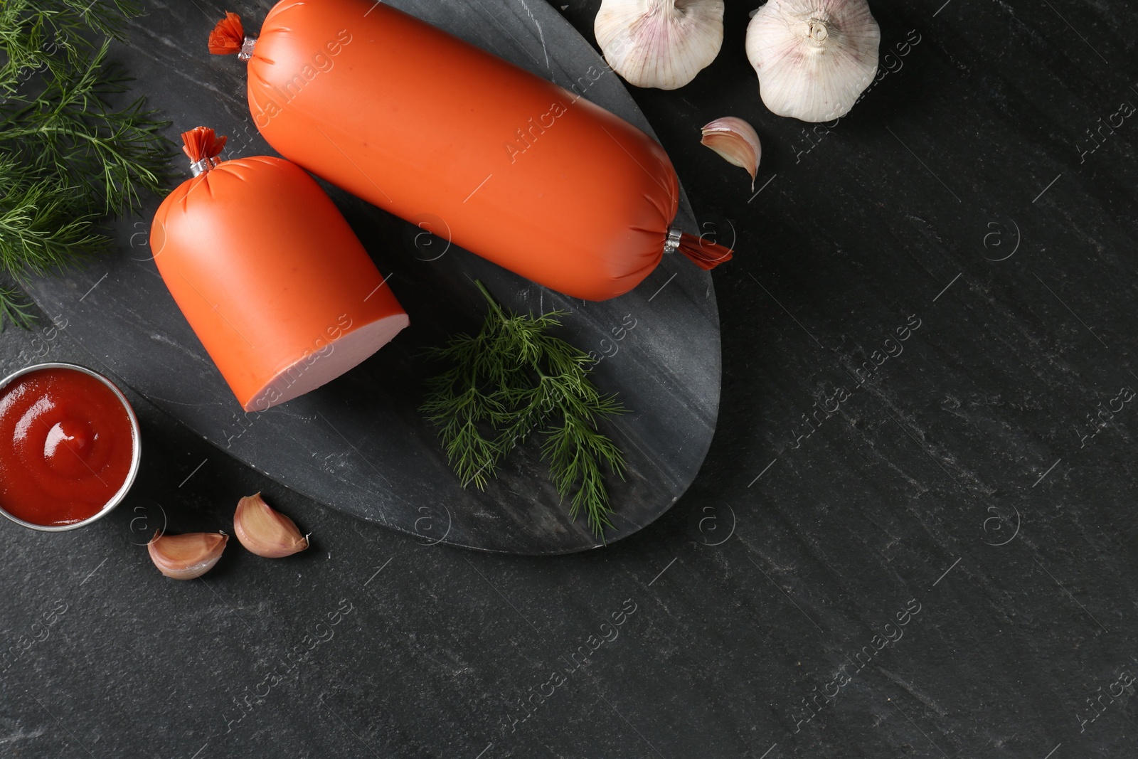 Photo of Tasty boiled sausages, ketchup, dill and garlic on black table, top view. Space for text