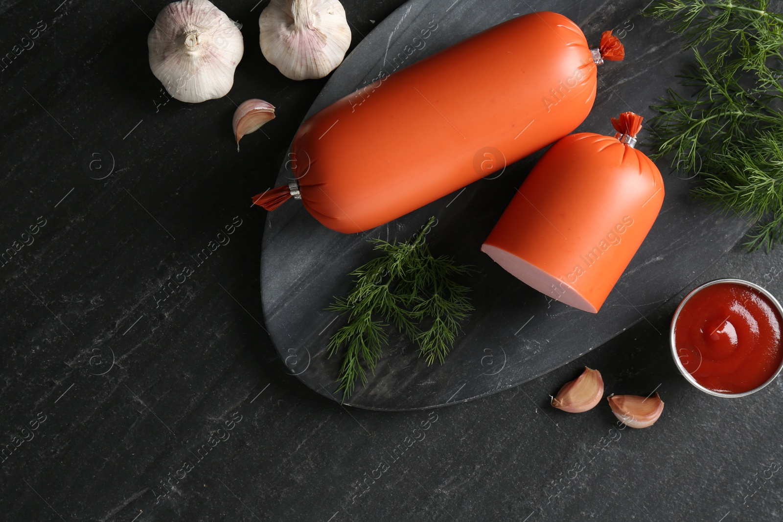 Photo of Tasty boiled sausages, ketchup, dill and garlic on black table, top view. Space for text