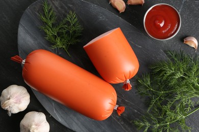 Photo of Tasty boiled sausages, ketchup, dill and garlic on black table, top view