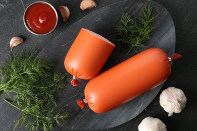 Photo of Tasty boiled sausages, ketchup, dill and garlic on black table, top view