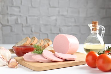 Photo of Tasty boiled sausage, spices, tomatoes, ketchup and bread on white table