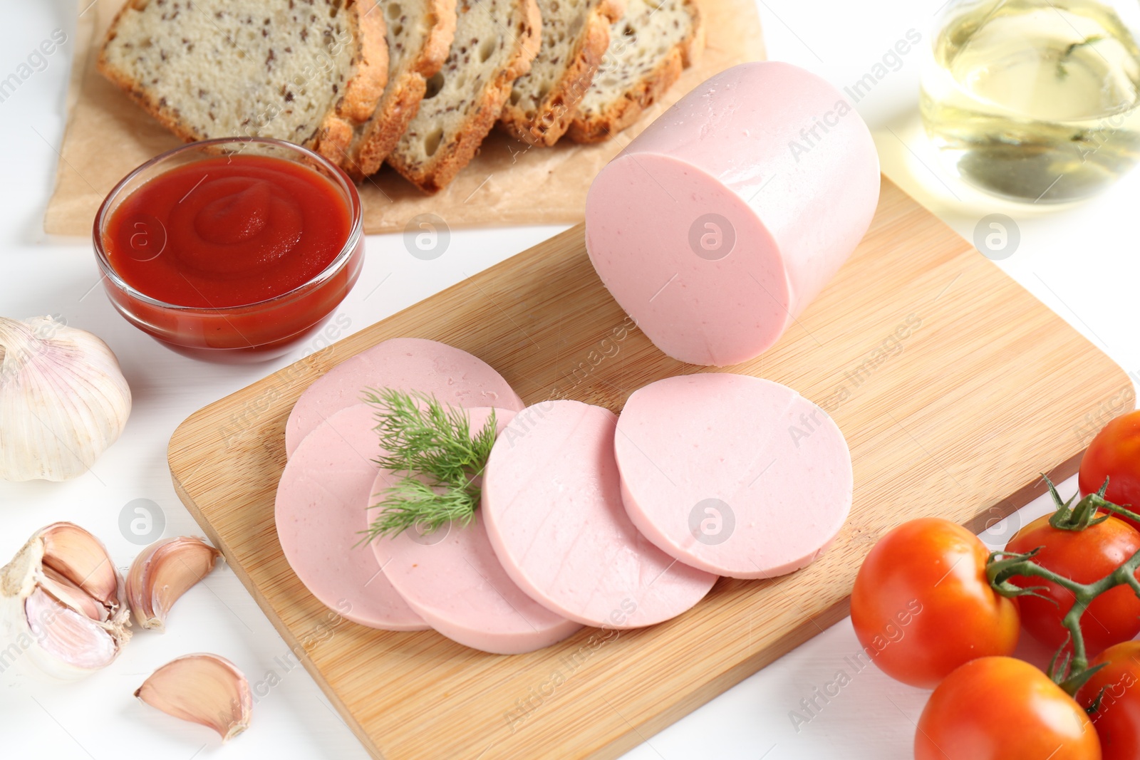 Photo of Tasty boiled sausage, spices, tomatoes, ketchup and bread on white table