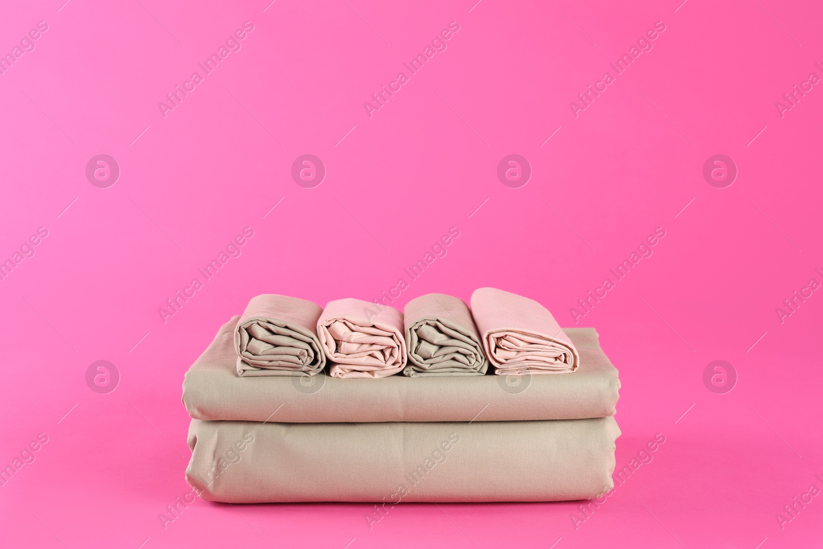 Photo of Stack of clean bed sheets on pink background