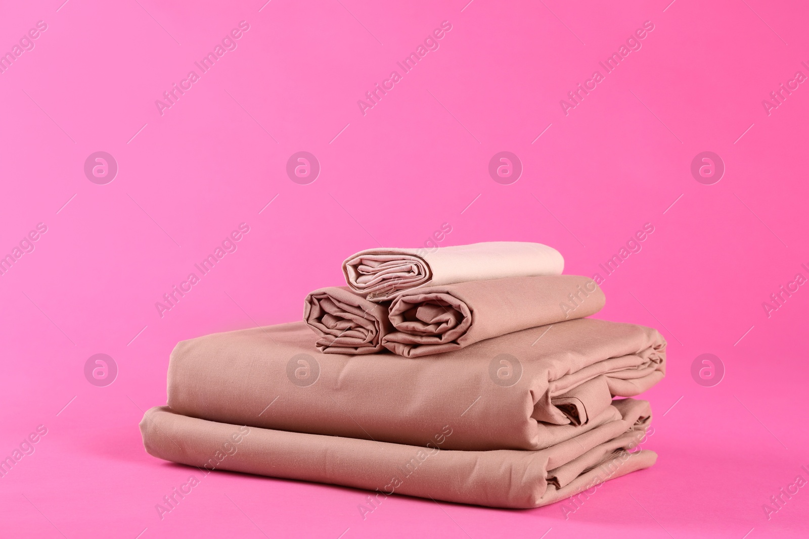 Photo of Stack of clean bed sheets on pink background