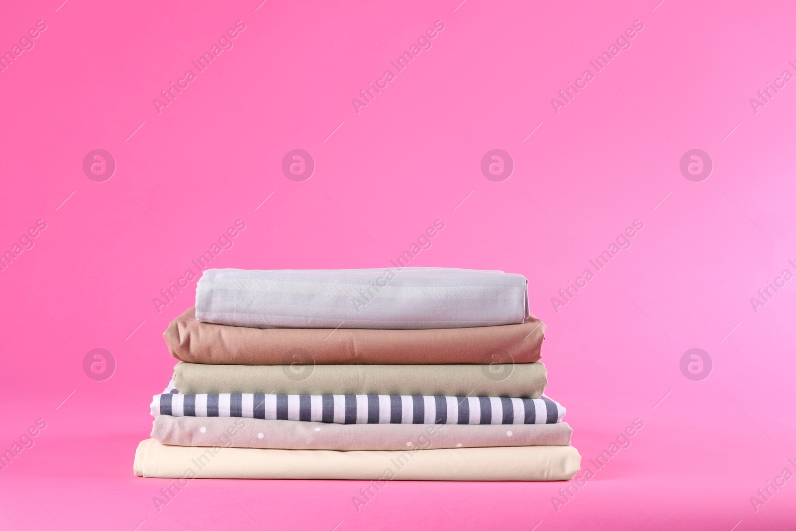 Photo of Stack of clean bed sheets on pink background. Space for text