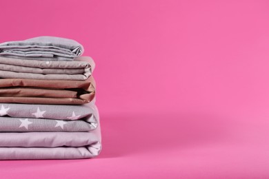 Photo of Stack of clean bed sheets on pink background. Space for text