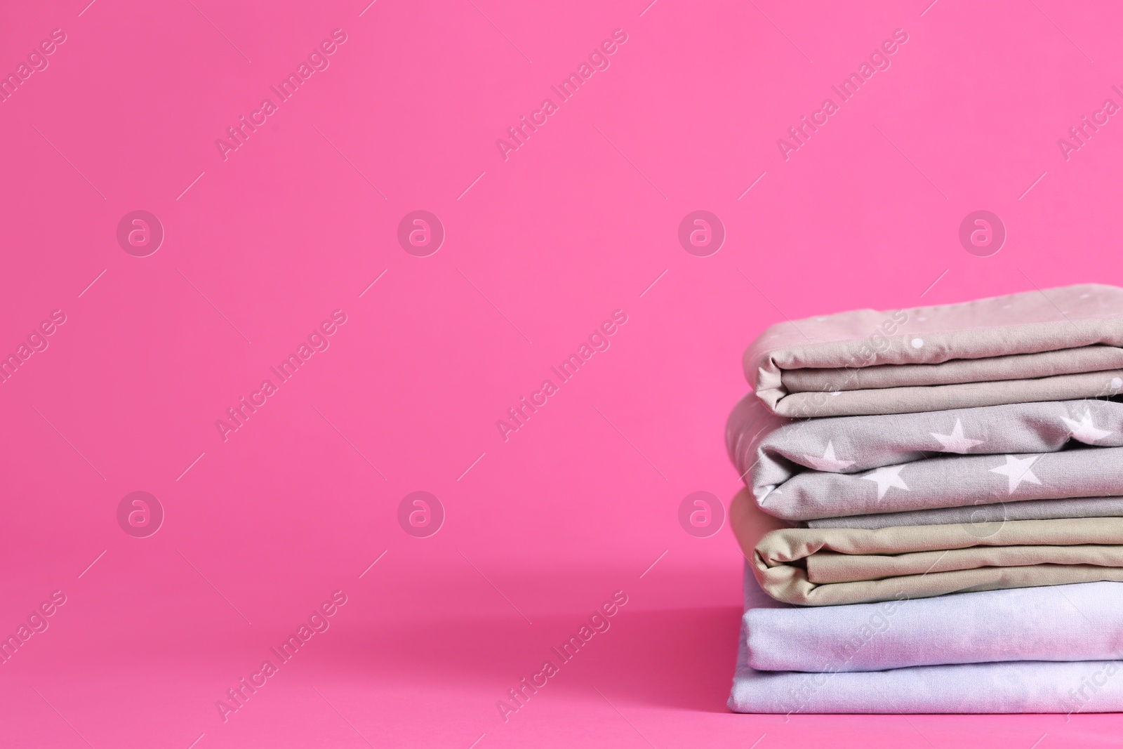 Photo of Stack of clean bed sheets on pink background. Space for text