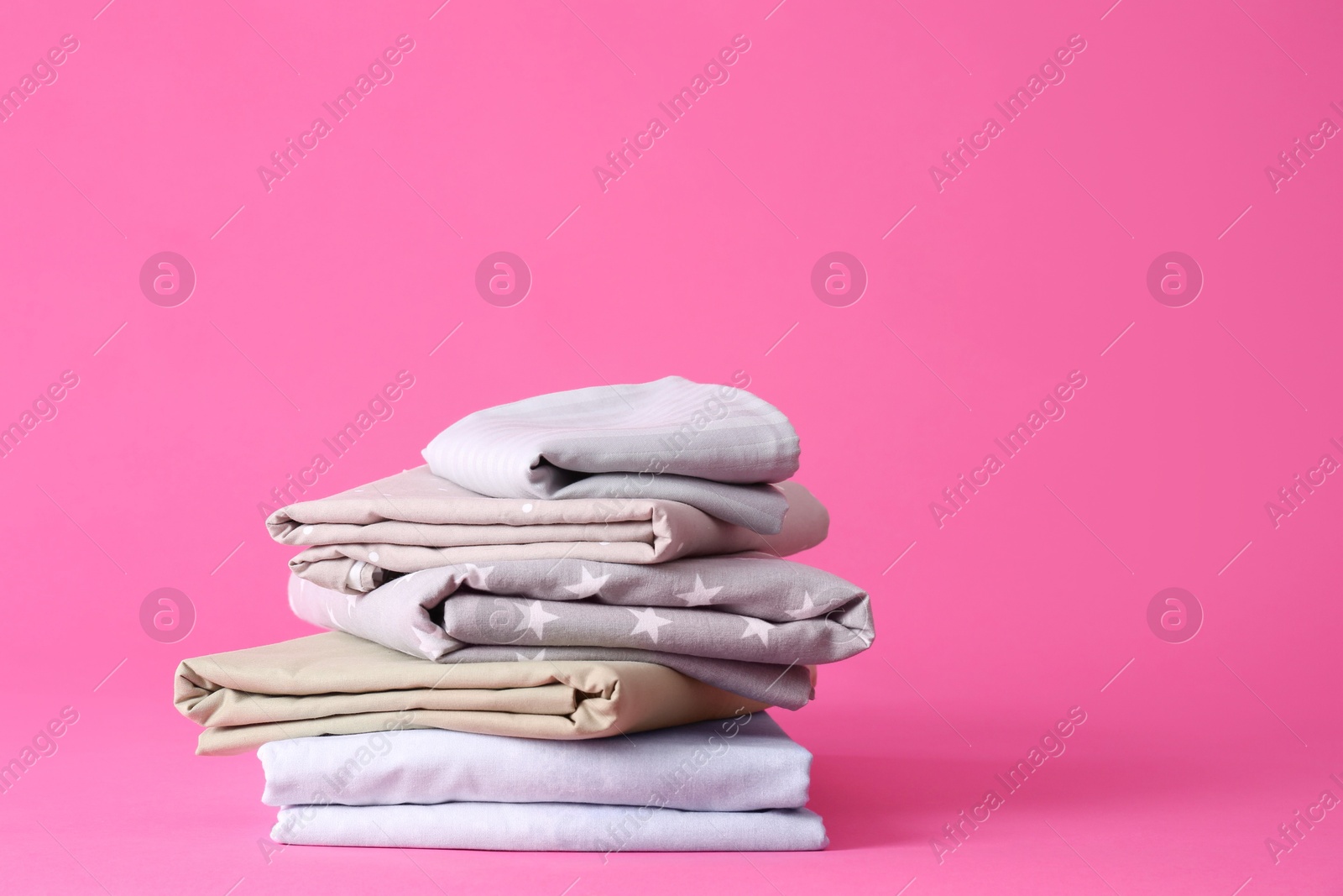 Photo of Stack of clean bed sheets on pink background. Space for text