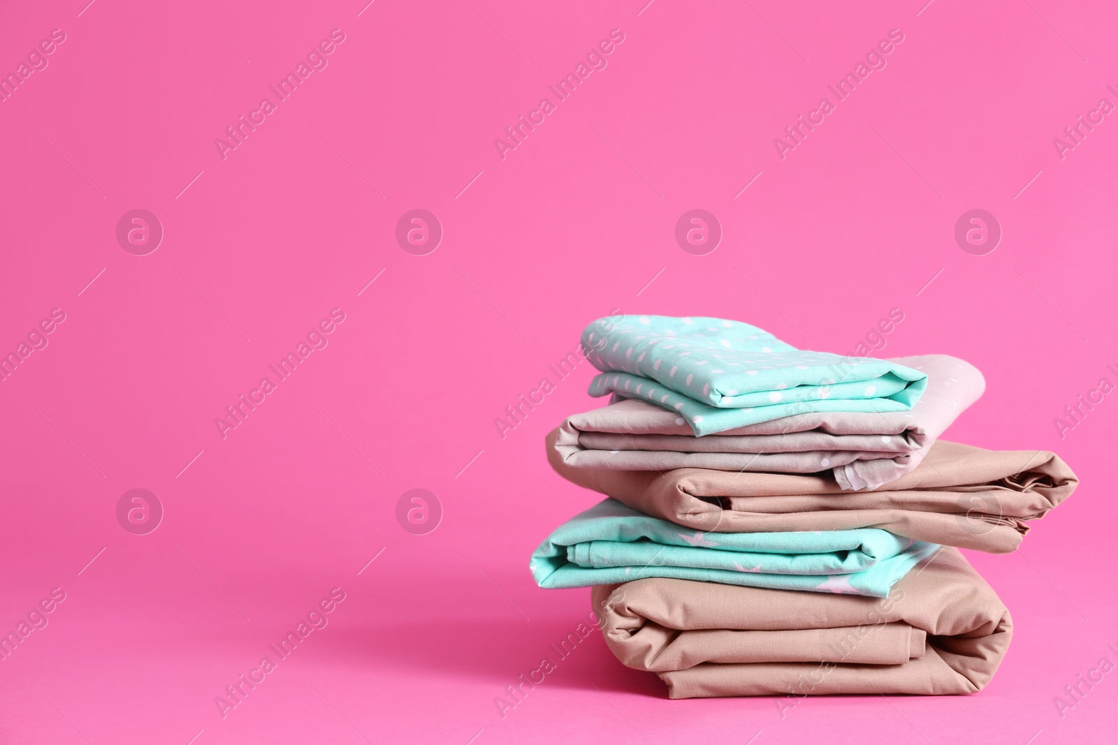 Photo of Stack of clean bed sheets on pink background. Space for text