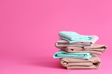 Photo of Stack of clean bed sheets on pink background. Space for text