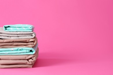 Photo of Stack of clean bed sheets on pink background. Space for text