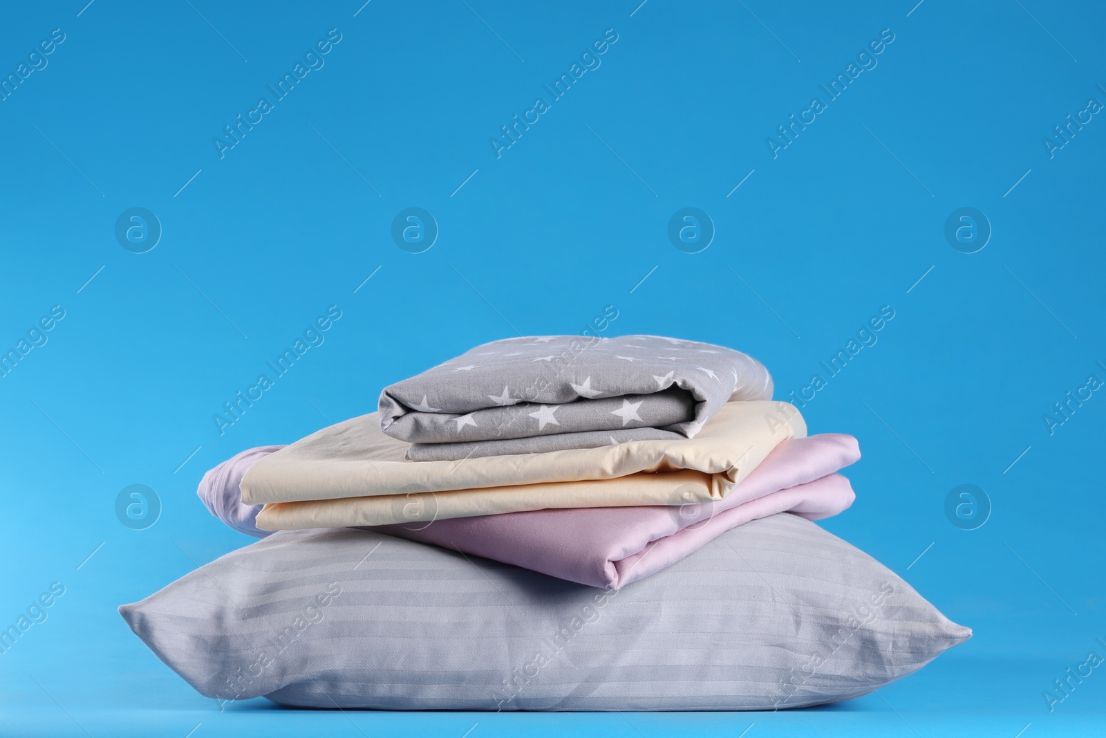 Photo of Stack of clean bed sheets and pillow on blue background