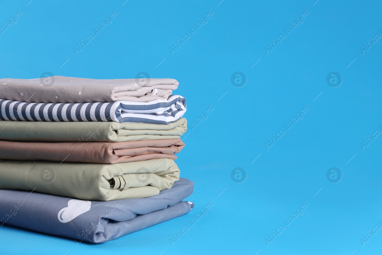 Photo of Stack of clean bed sheets on blue background. Space for text