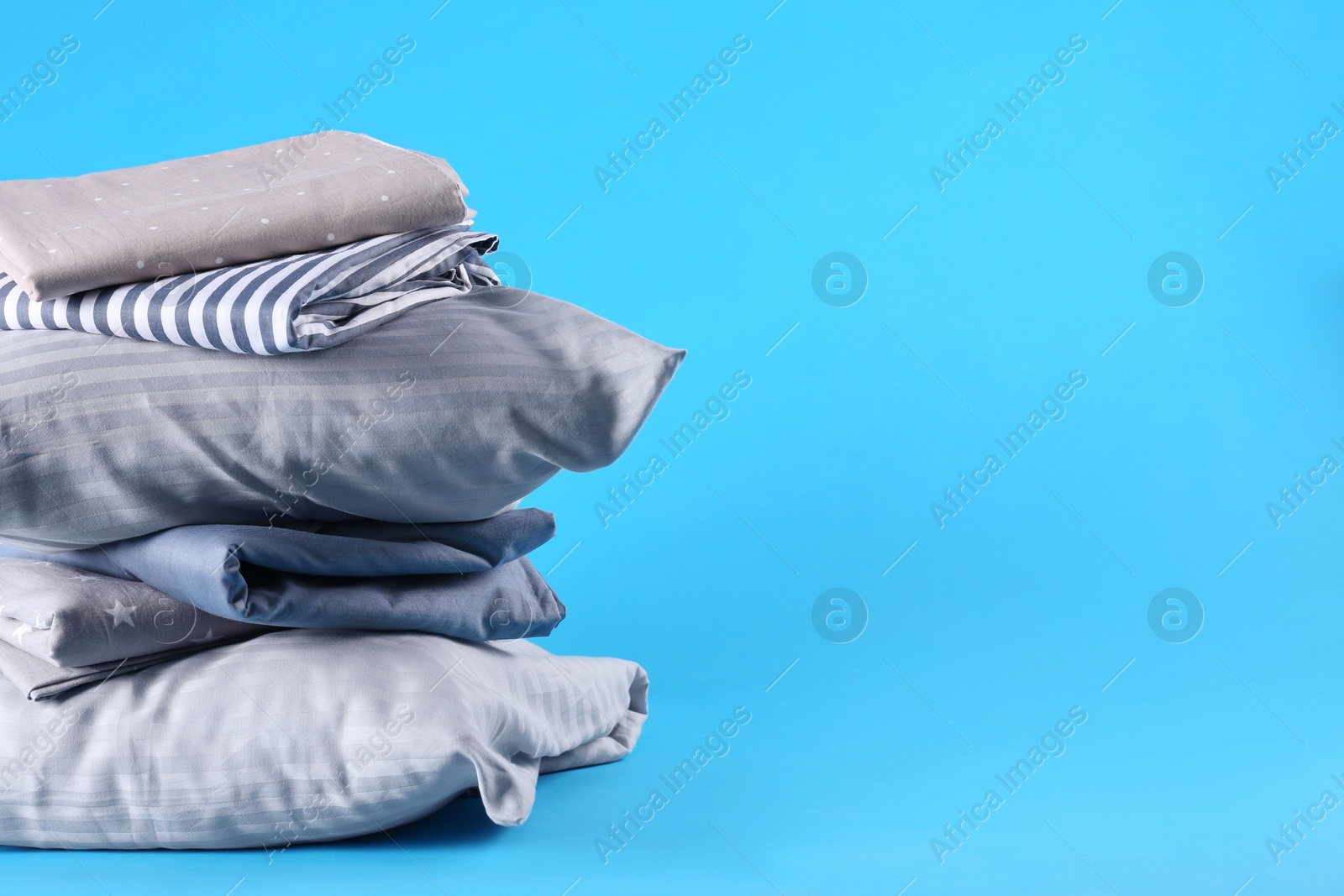 Photo of Stack of clean bed sheets and pillows on blue background. Space for text