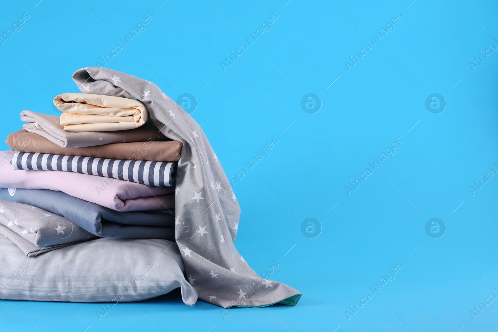 Photo of Stack of clean bed sheets and pillow on blue background. Space for text