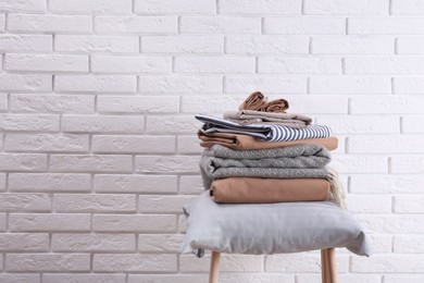 Photo of Stack of clean bed sheets and pillow on stool near white brick wall. Space for text