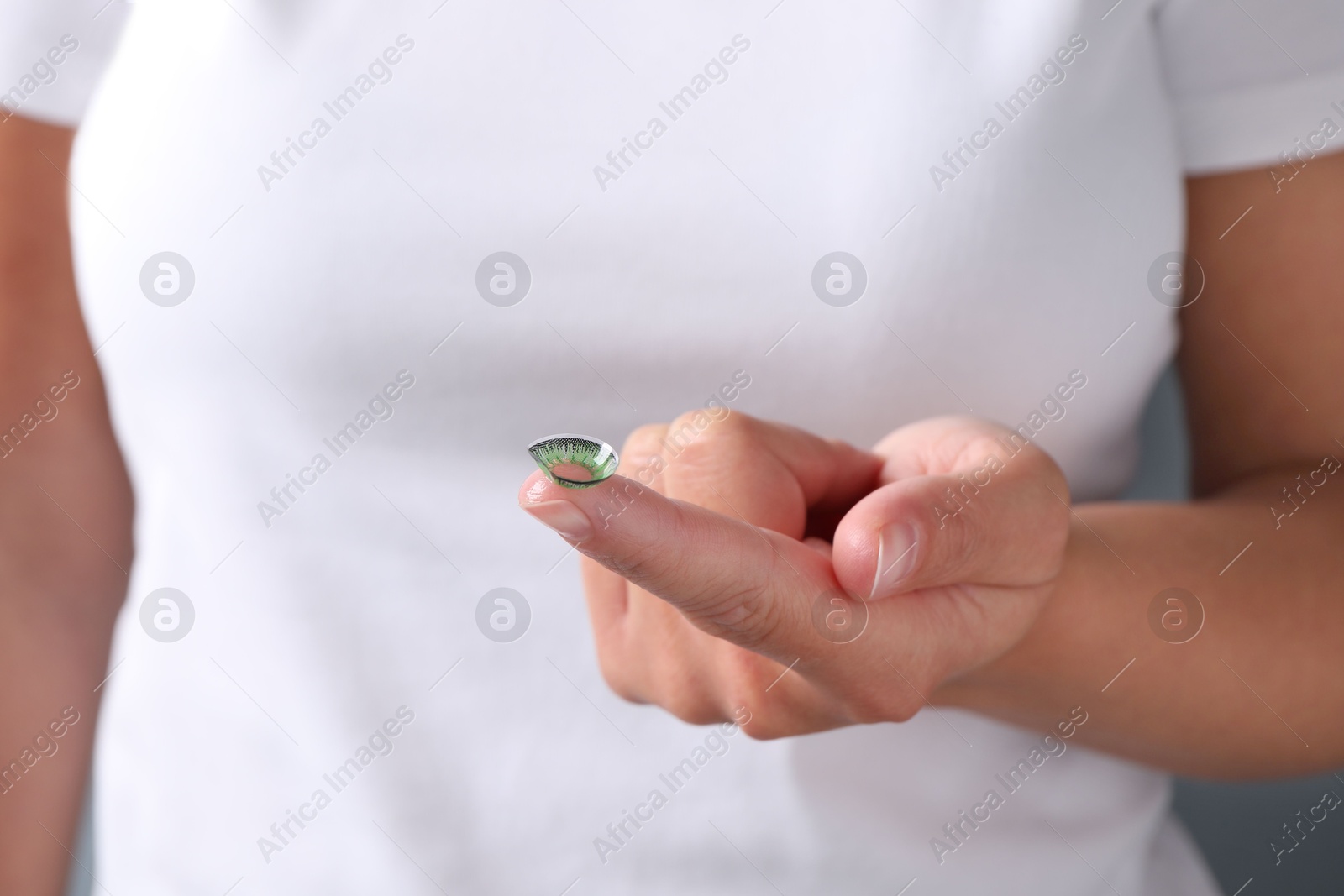 Photo of Woman holding color contact lens on light background, closeup