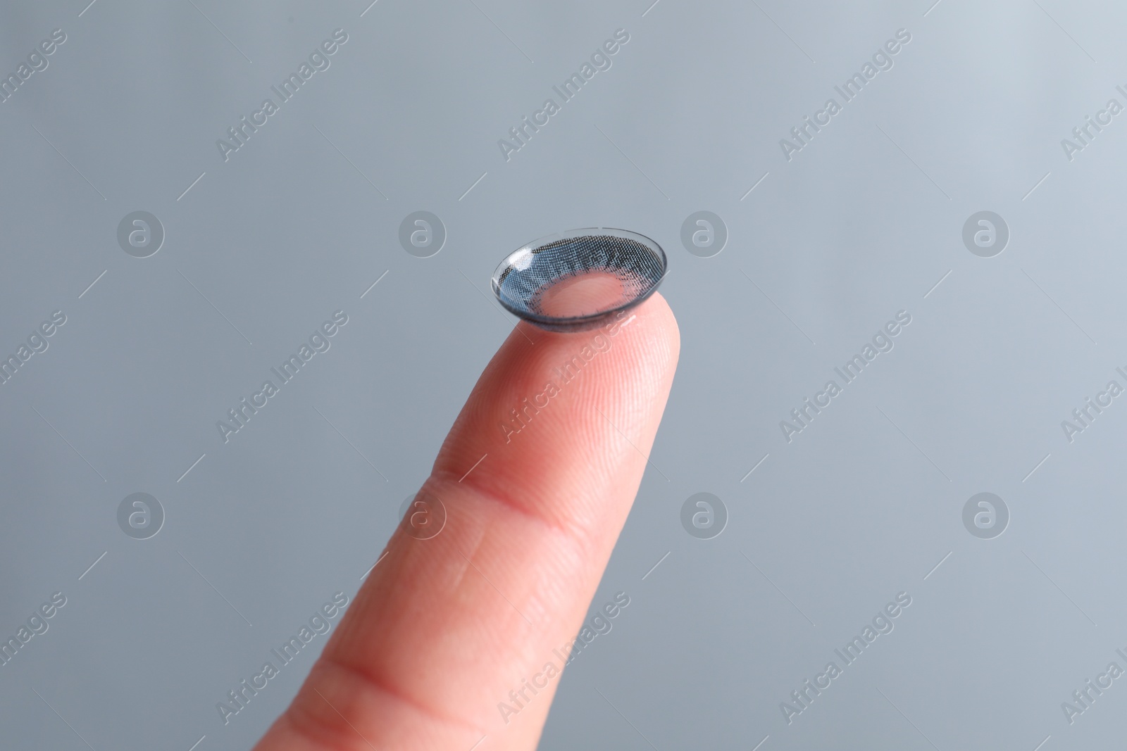 Photo of Woman holding color contact lens on light grey background, closeup